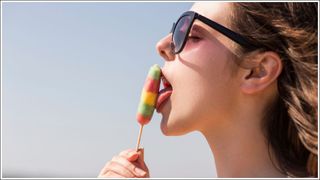 Side view of seductive woman licking ice lolly against clear sky