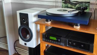 The DALI Rubikore 2 speaker next to a record player and a wooden surface.