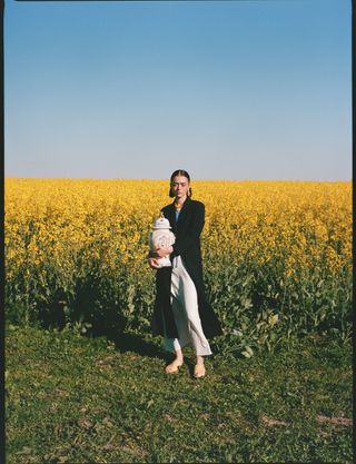 woman standing in a field of yellow flowers, holding a vase