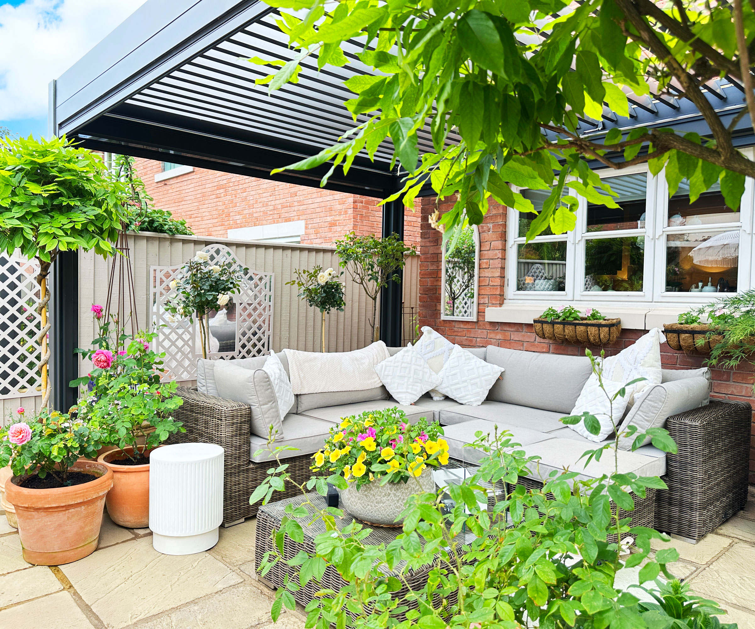 modern pergola on patio with modular L shaped garden sofas and planting including flowers and clipped trees