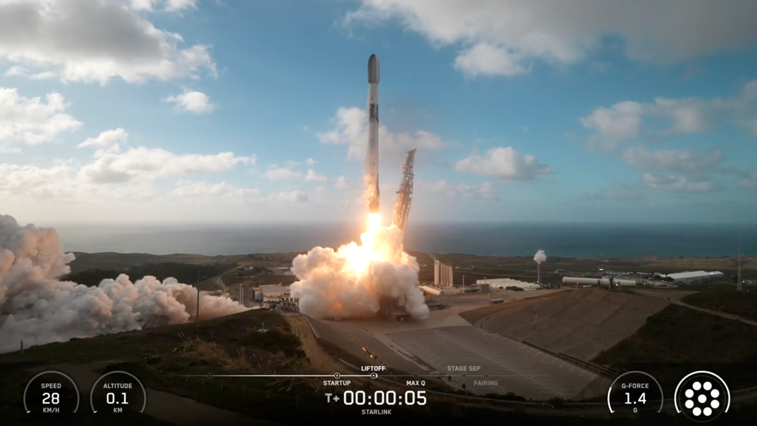 a black and white rocket launches into a blue sky from a seaside pad
