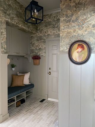 gray color-drenched mudroom with a built-in bench and pattered wallpaper on the top half of the wall