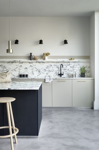 White marble kitchen worksurface and backsplash in a white scheme with midnight blue painted kitchen island.
