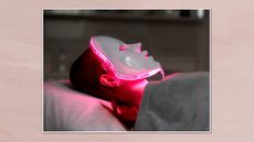 Image of woman wearing a red light therapy mask in a white frame against a dusky pink background