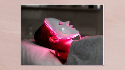 Image of woman wearing a red light therapy mask in a white frame against a dusky pink background