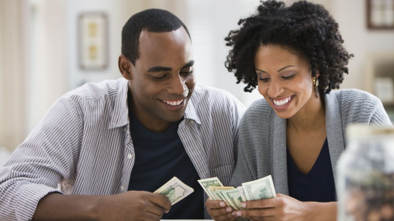 A couple smile as they look down at the cash they&#039;re holding.