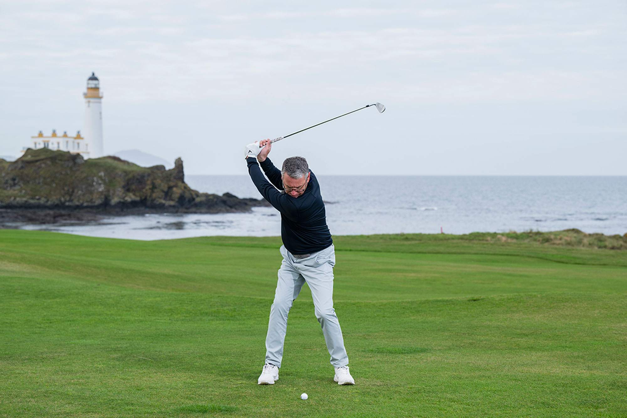Steve North at the top of his backswing, preparing to hit an iron shot in windy conditions at Turnberry