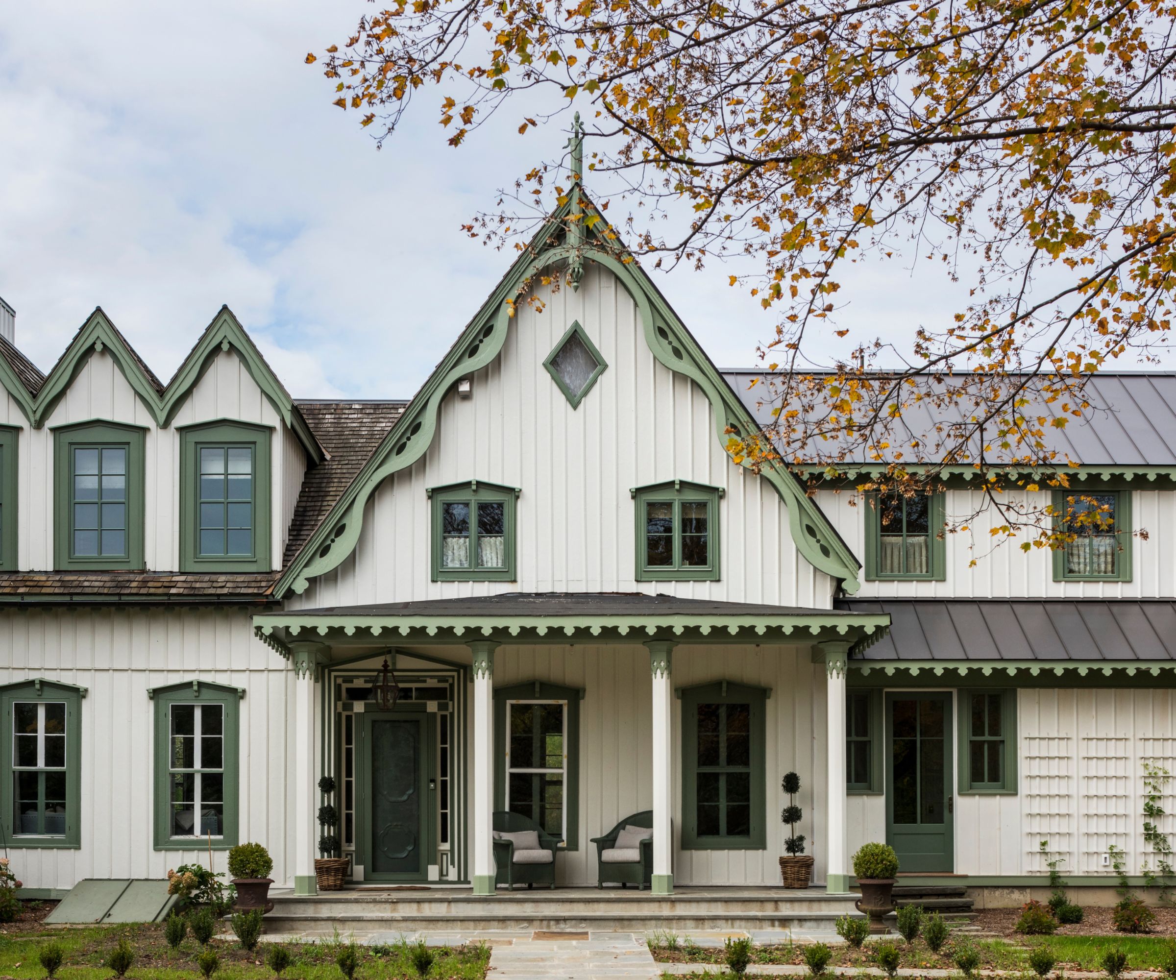 A historic home exterior with warm white wood, mid-toned green trim, and a porch with pillars.
