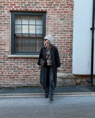 Woman wears navy long coat, grey beanie, camel jumper and blue jeans.