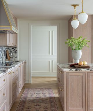 kitchen with marble backsplash vintage rug and pale wood cabinets