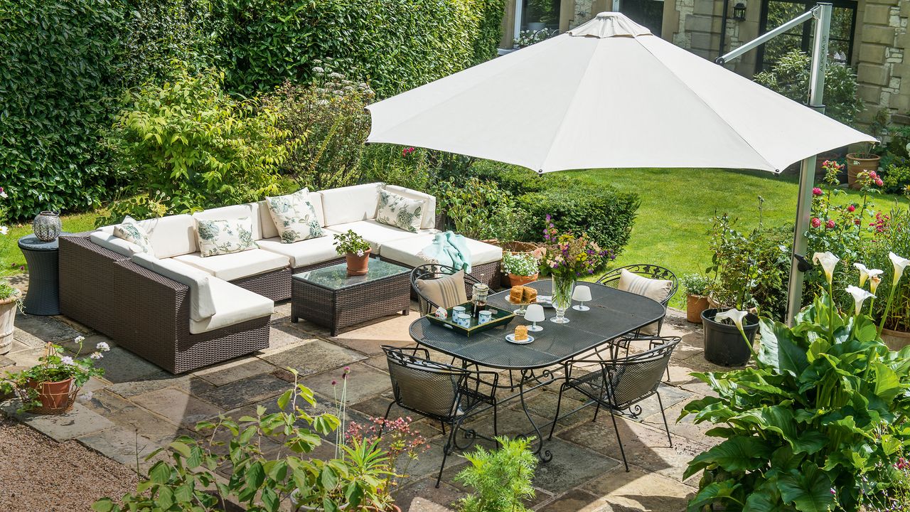 patio area in a garden with a large parasol, table and chairs and lots of planting and raised beds