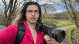 OM System M.Zuiko 150-600mm f/5.0-6.3 IS lens, mounted to an OM System OM-1 Mark II, being held by photographer James Artaius in a woodland setting