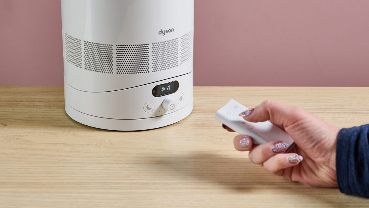 A woman is pointing the remote at the Dyson Cool F1 while changing the fan speed.
