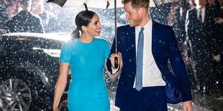 Meghan Markle and Prince Harry shelter under a shared umbrella as they walk through the rain.