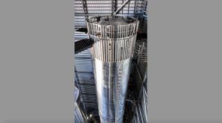 a shiny silver rocket booster sits in a building with corrugating tin walls