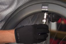 Cyclist wearing gloves for protection from the cold CO2 canister using a Topeak Micro Airbooster to inflate a road tyre on a DT Swiss rim