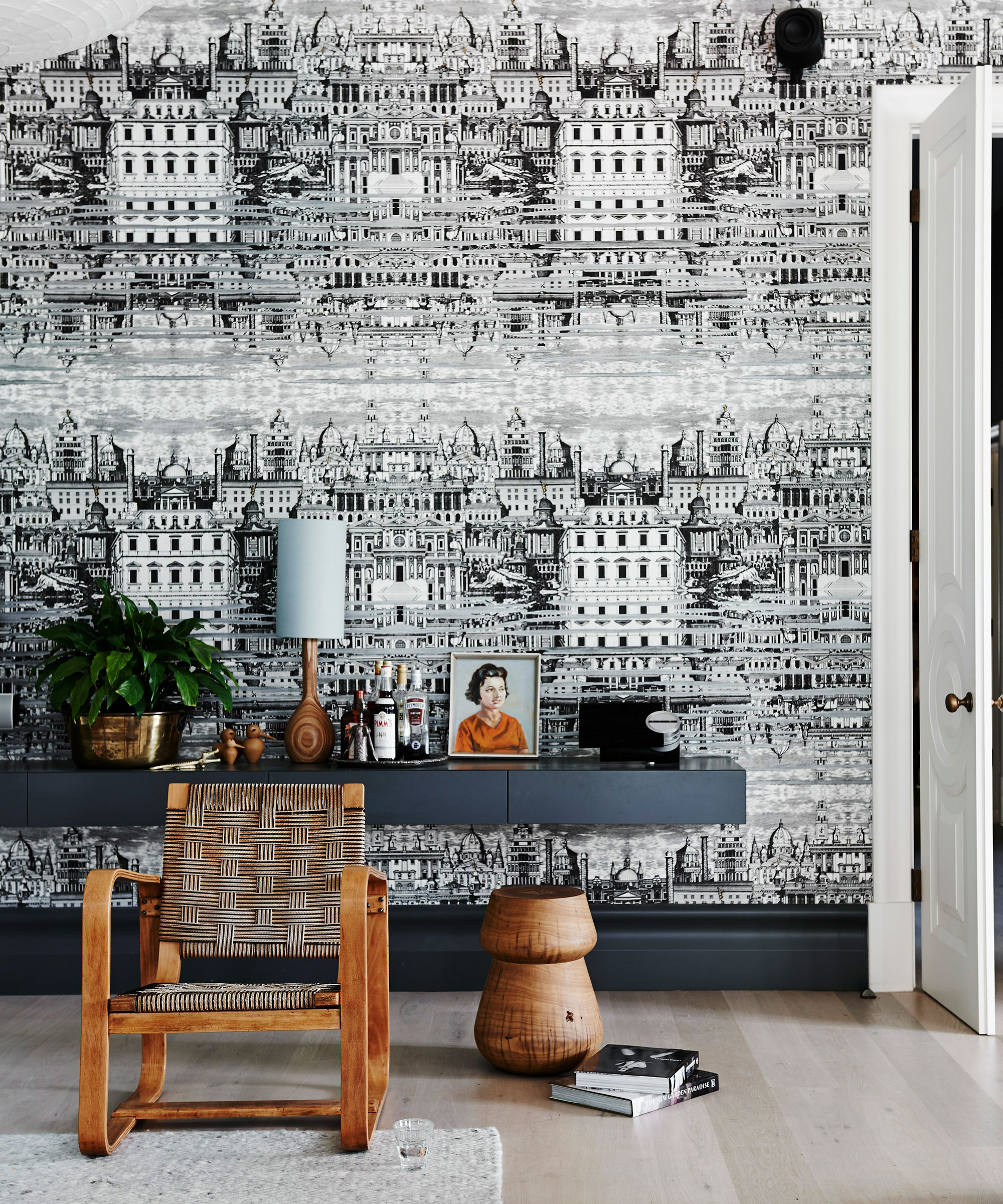 A black living room with monochrome architectural print wallpaper, open shelving and a wooden chair.