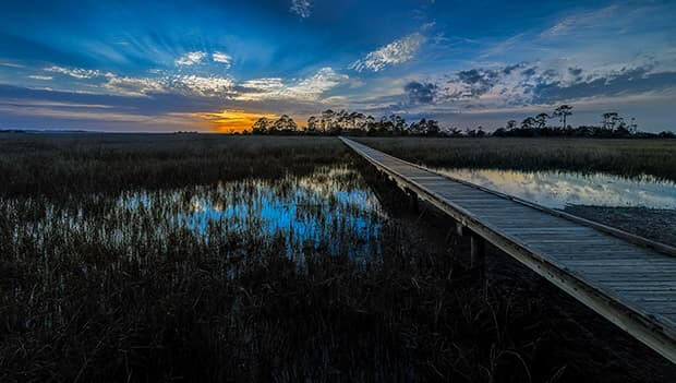 Wooden walkway crossing a body of water at sunset.