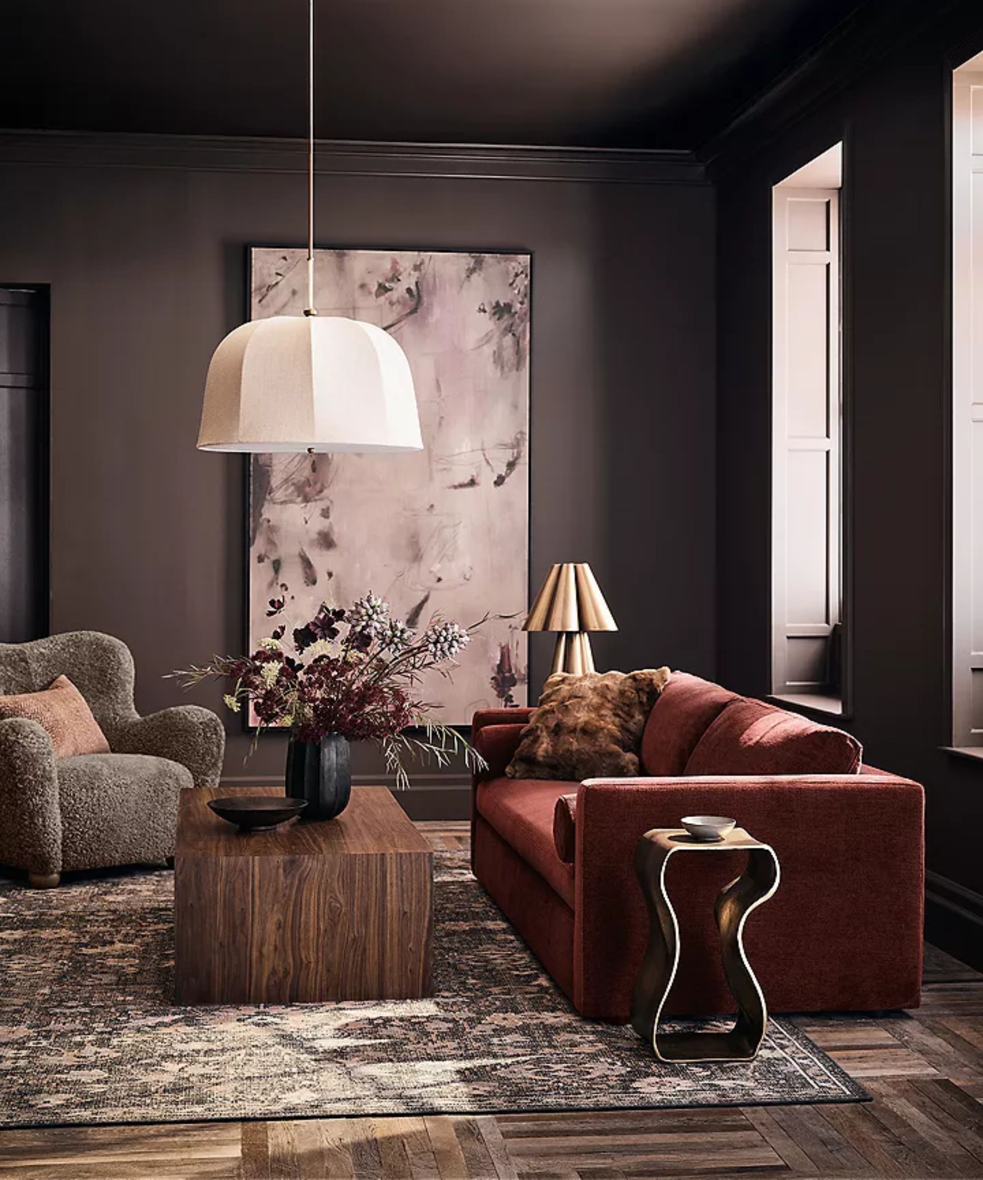 dark brown living room with large artwork, pendant light, a wooden coffee table and dark red velvet couch