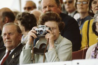 Queen Elizabeth II at The Windsor Horse Show, 16th May 1982. She is taking pictures of her husband with her Leica M3 camera.