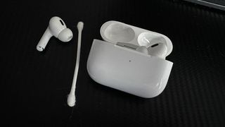 AirPods next to the charging case and a cotton swab.