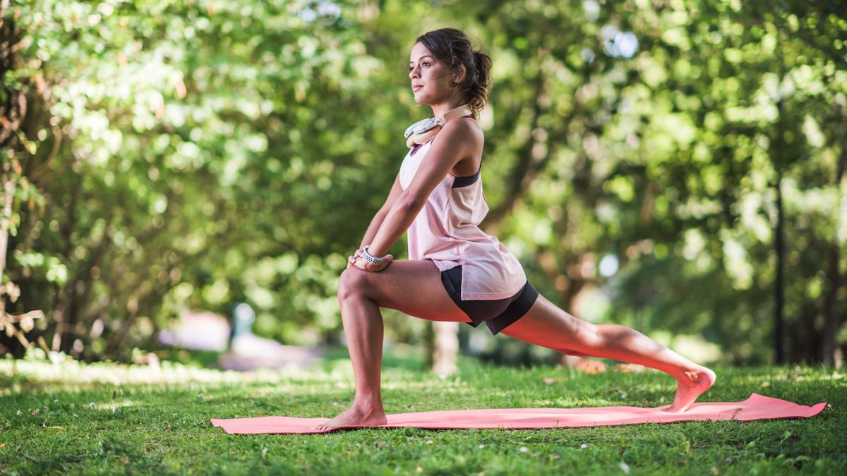 A woman does yoga outside surrounded by trees