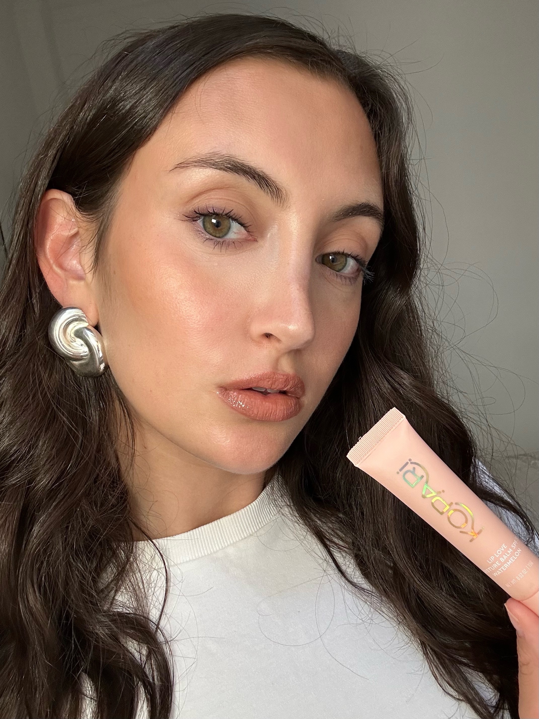 An image of Alyssa Brascia wearing and holding the Kopari Lip Love Moisture Balm.
