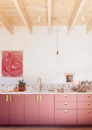 Metallic gold accents in a dusk pink kitchen with artwork hanging on the all and a speckled countertop.