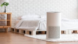 An air purifier in a bedroom in front of a bed and bedside cabinet