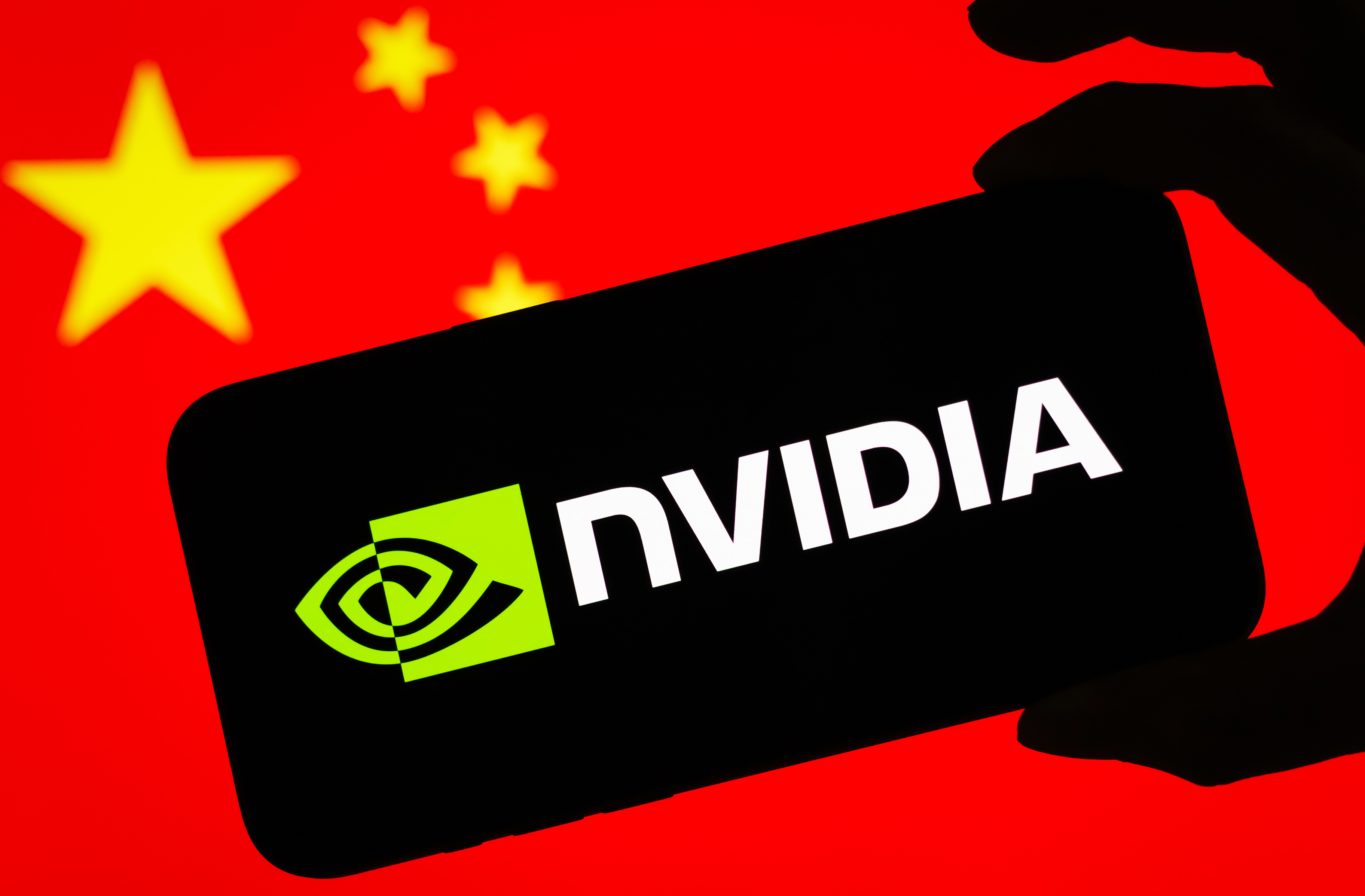 CHONGQING, CHINA - JULY 17: In this photo illustration, a smartphone displaying the logo of Nvidia Corporation (NASDAQ: NVDA), a leading American semiconductor and artificial intelligence company, is held in front of a screen showing the national flag of China on July 17, 2025 in Chongqing, China. (Photo illustration by Cheng Xin/Getty Images)