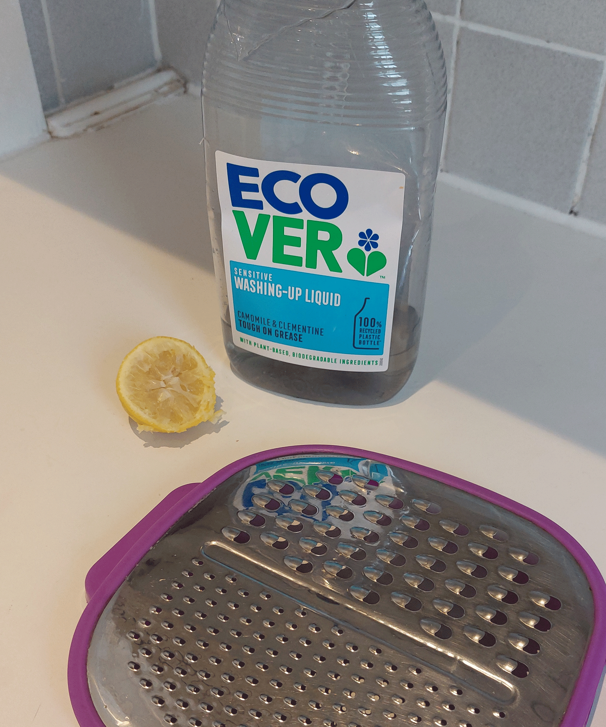 cheese grater, dish soap and a lemon on a kitchen worktop