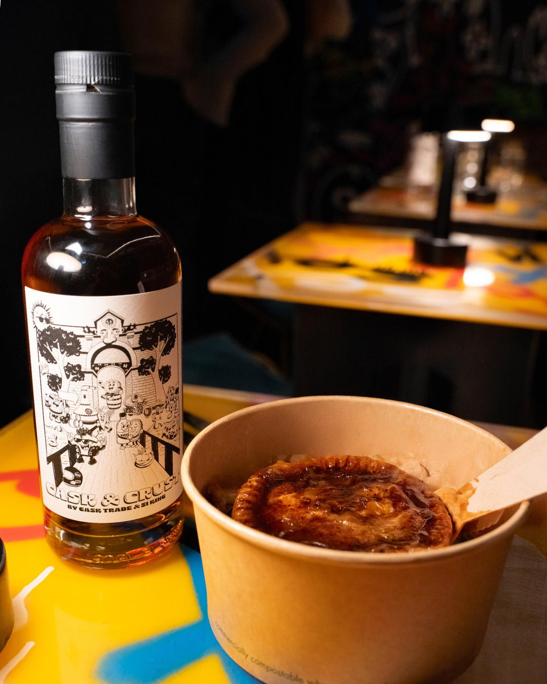 A bottle of Cask and Crust whisky next to a propa pie. there is lots of gravy