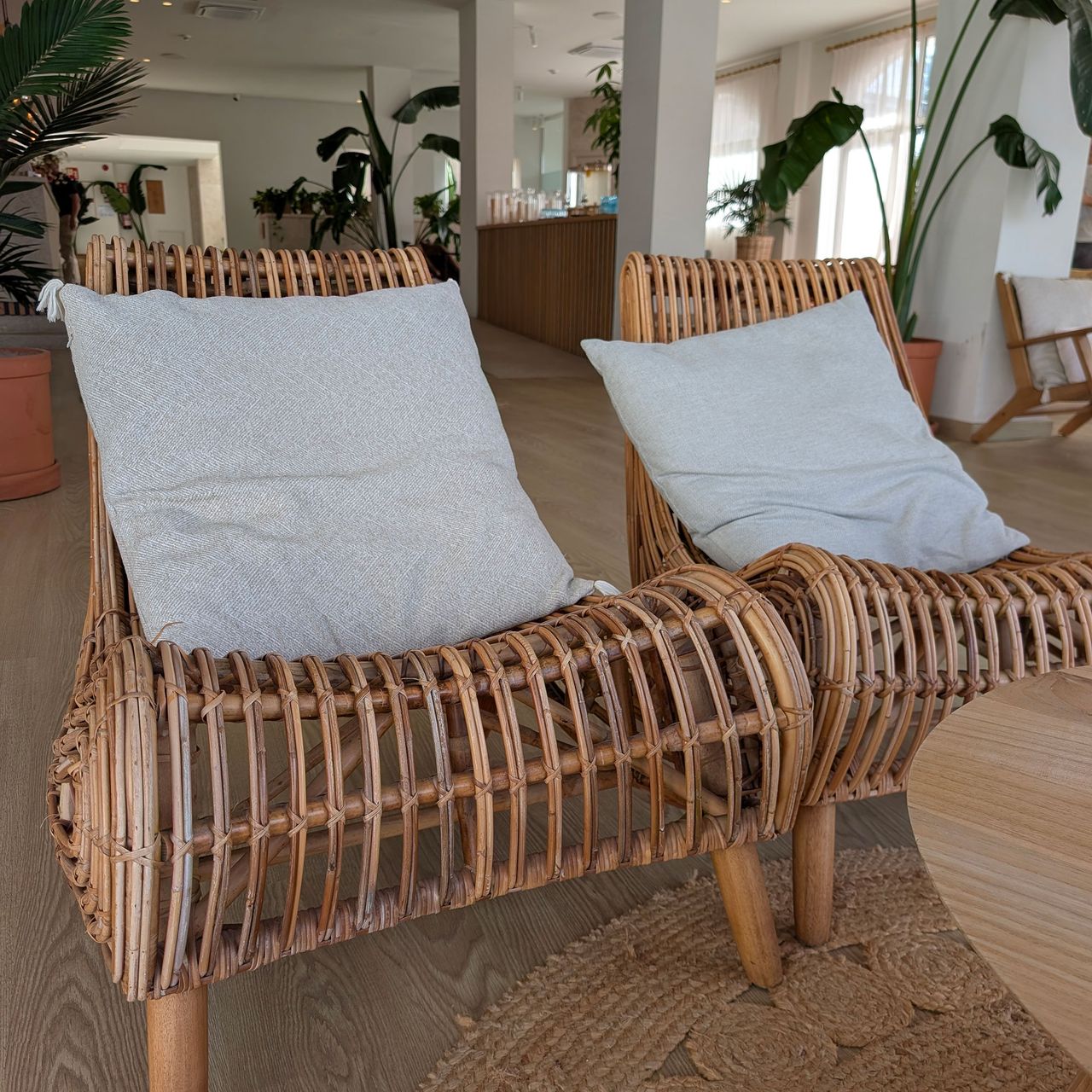 Two large wicker armchairs with grey cushions on jute rug in lounge area