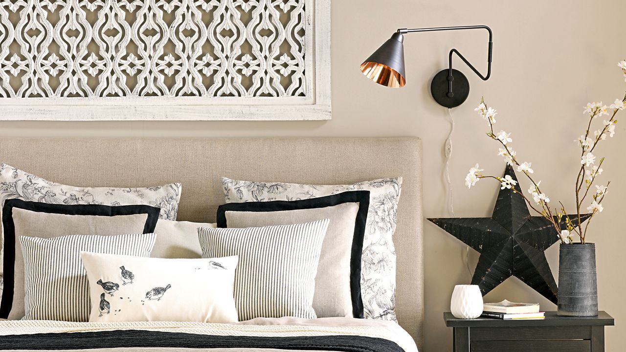 Beige bedroom with double bed with upholstered headboard and black accents including an angled wall light