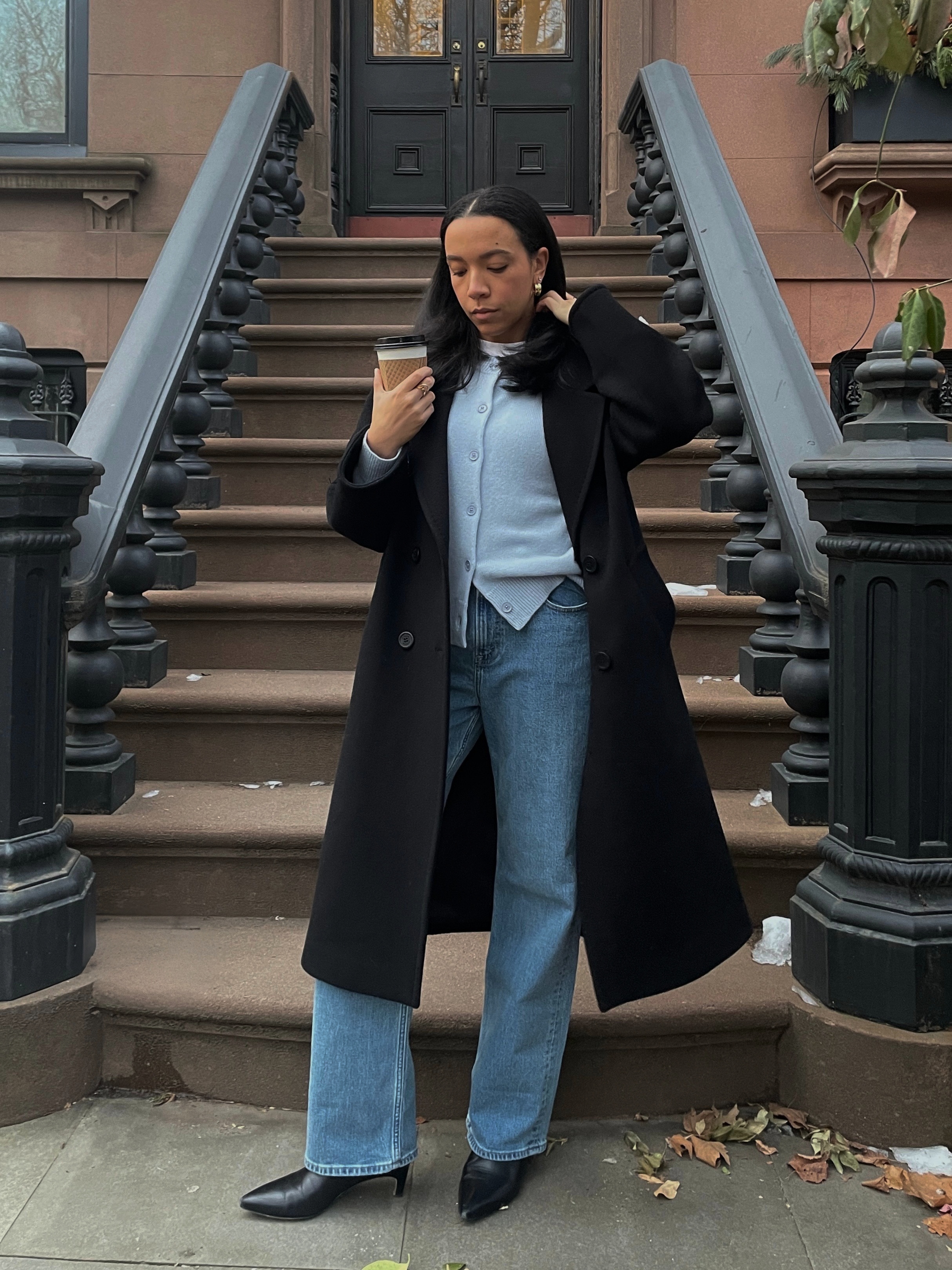 Lauren Tappan wearing a blue sweater, a black coat, jeans, and black boots