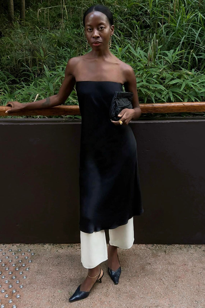 A French woman wearing a strapless black dress over white pants, and a pair of black slingback heels