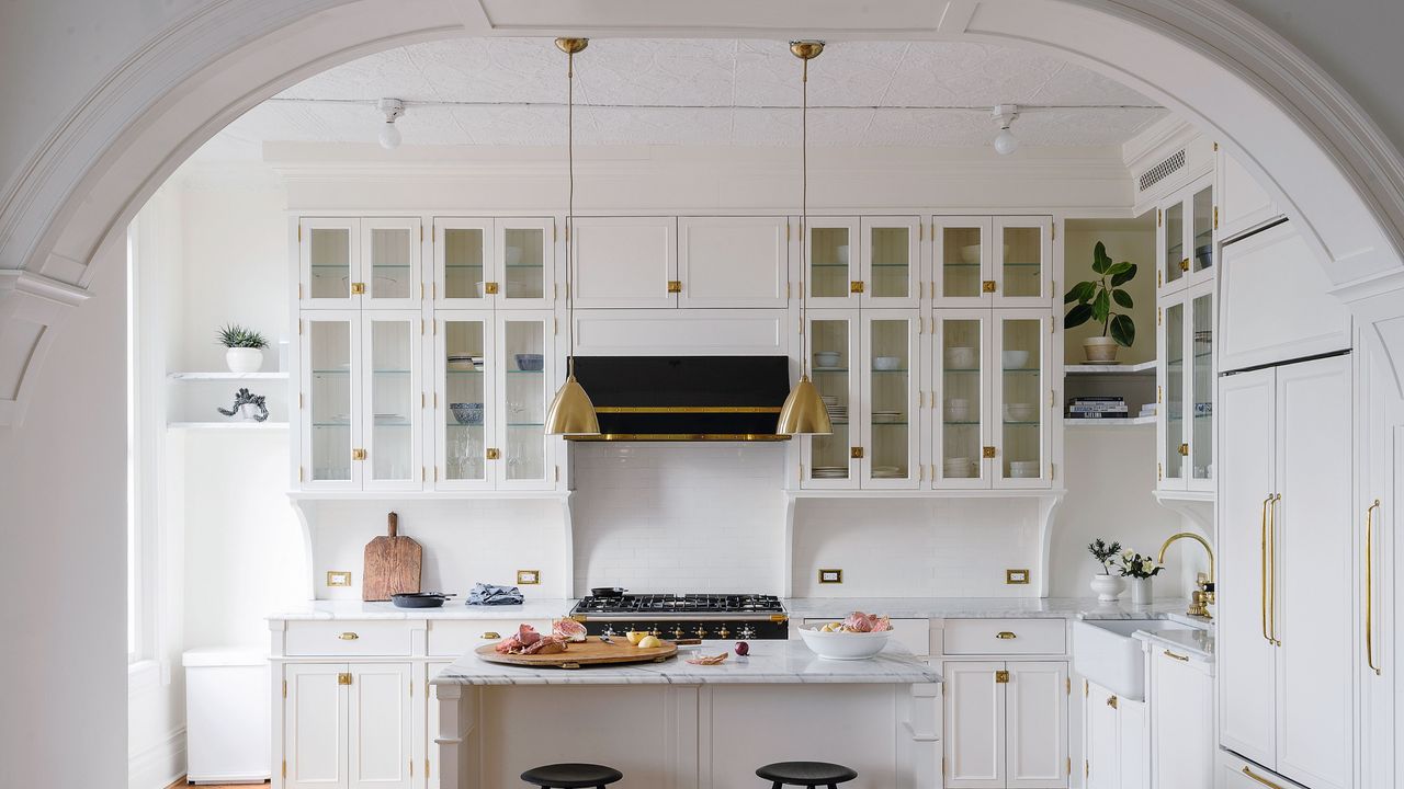 Fitted white country kitchen through period archway with kitchen island and brass fittings on parquet floor