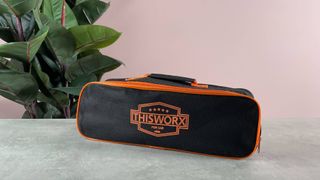 There is a black and orange storage bag on a grey stone surface with ThisWorx printed on the front.