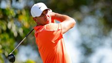 Brooks Koepka wearing an orange polo and white Nike cap while holding his finish on a fairway wood shot