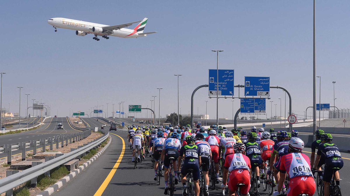 The peloton cycles through Dubai as a plane flies overhead.