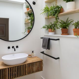 bathroom with white wall round mirror and plant on wooden shelf