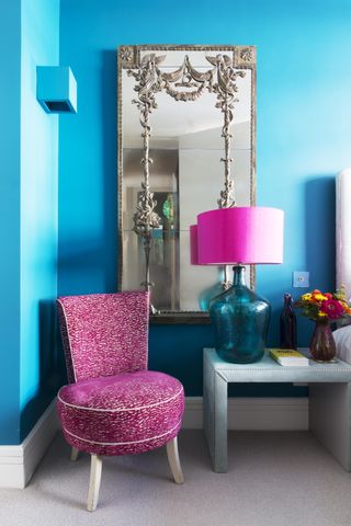 A bedroom with bright blue walls and a bright pink chair