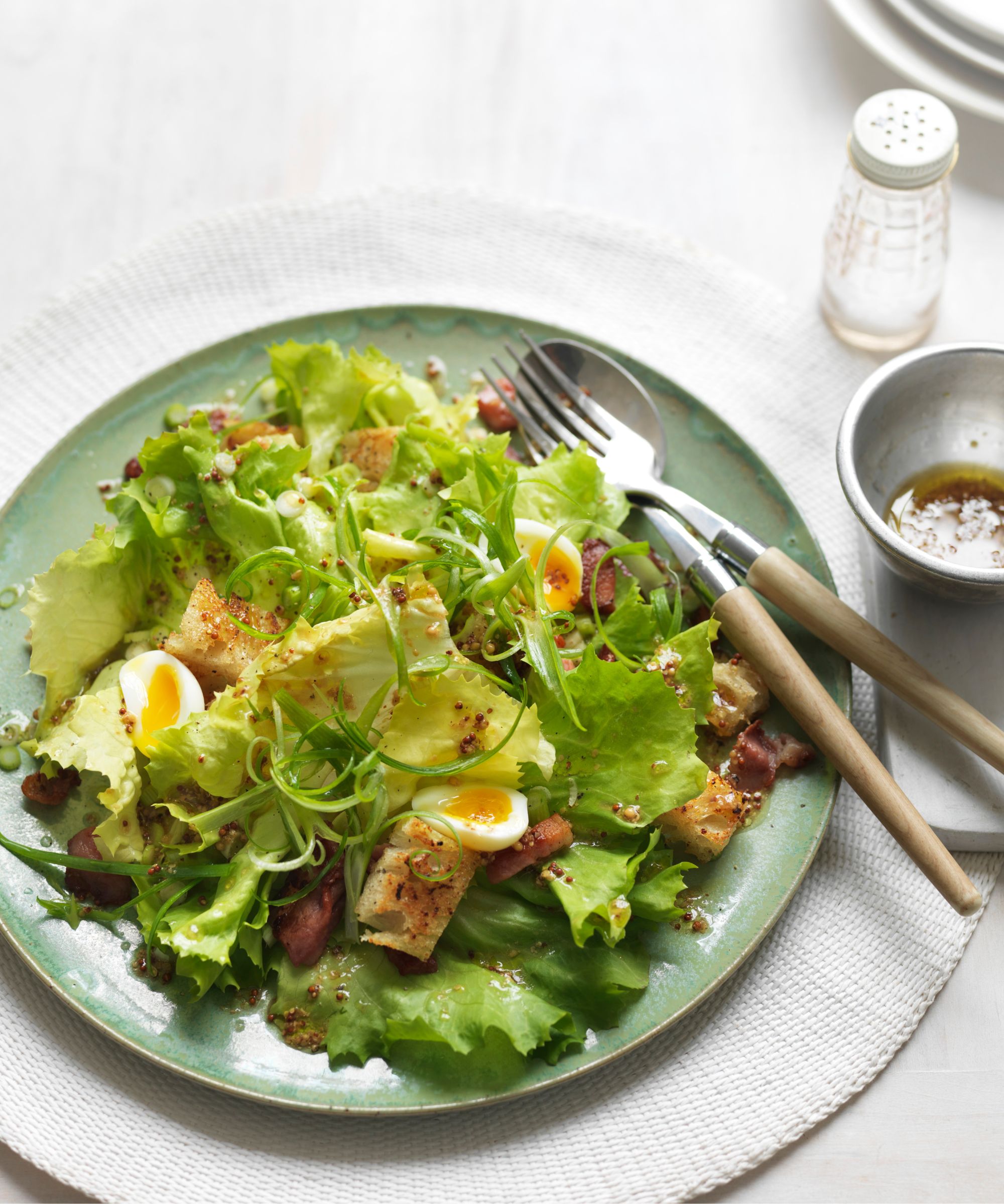 Egg salad on a green plate with cutlery and a bowl of dressing on the side