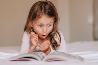 Little girl reading a book with an excited, animated expression on her face