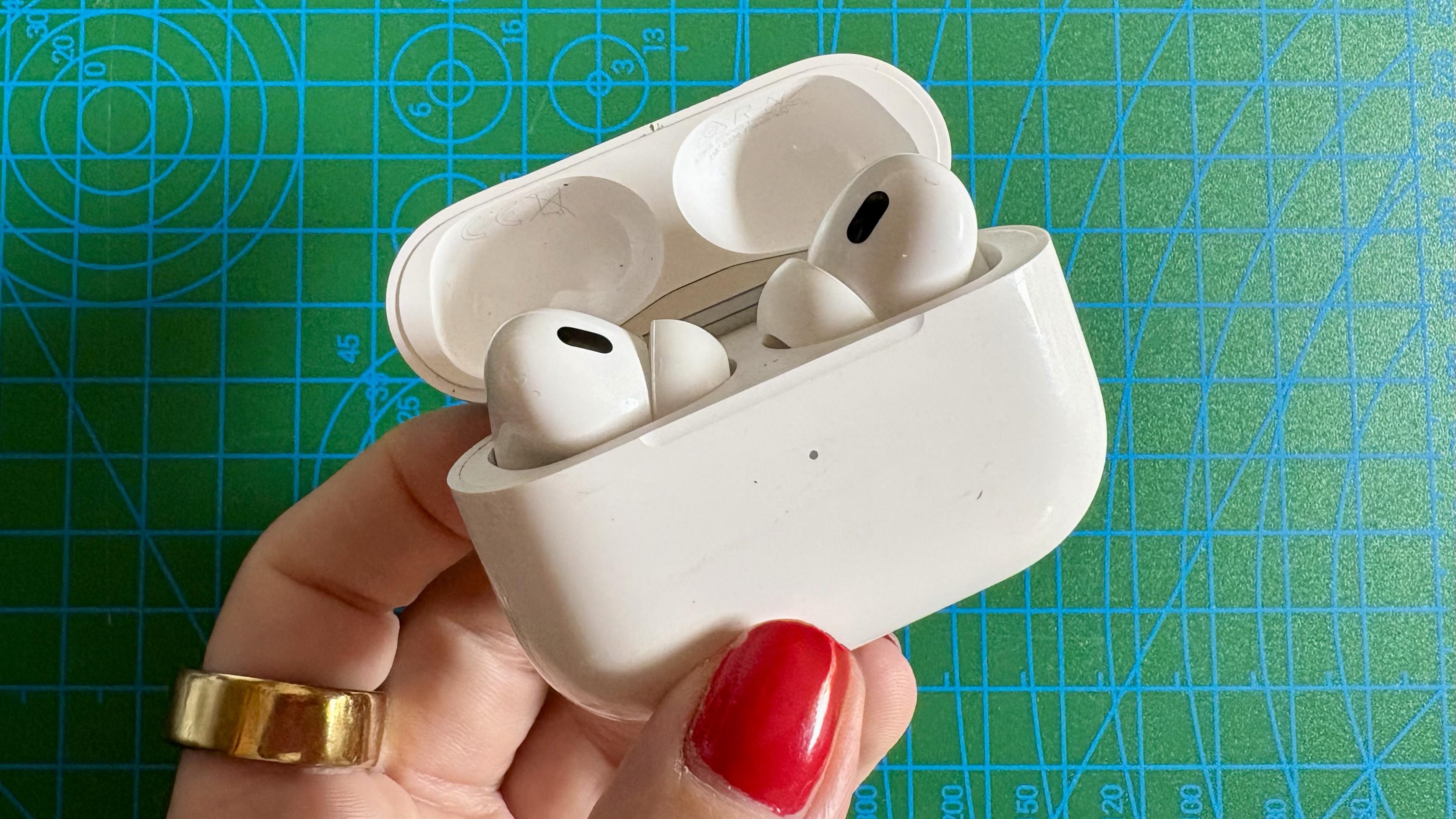 Person holding the Apple AirPods Pro 2 in front of a green background