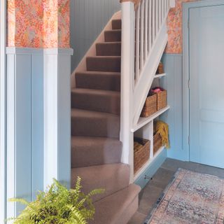 Under stairs built-in storage in a hallway with blue panelling and coral wallpaper.