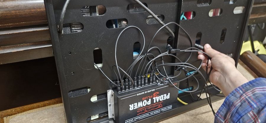 A man attaches a power supply to the underside of the Voodoo Lab Dingbat Medium pedalboard