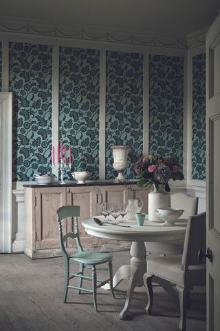 classic dining room with wallpaper between panels, white table, painted chairs, antique sideboard