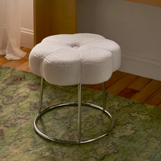 A boucle flower-shaped stool with silver hardware on a green patterned carpet