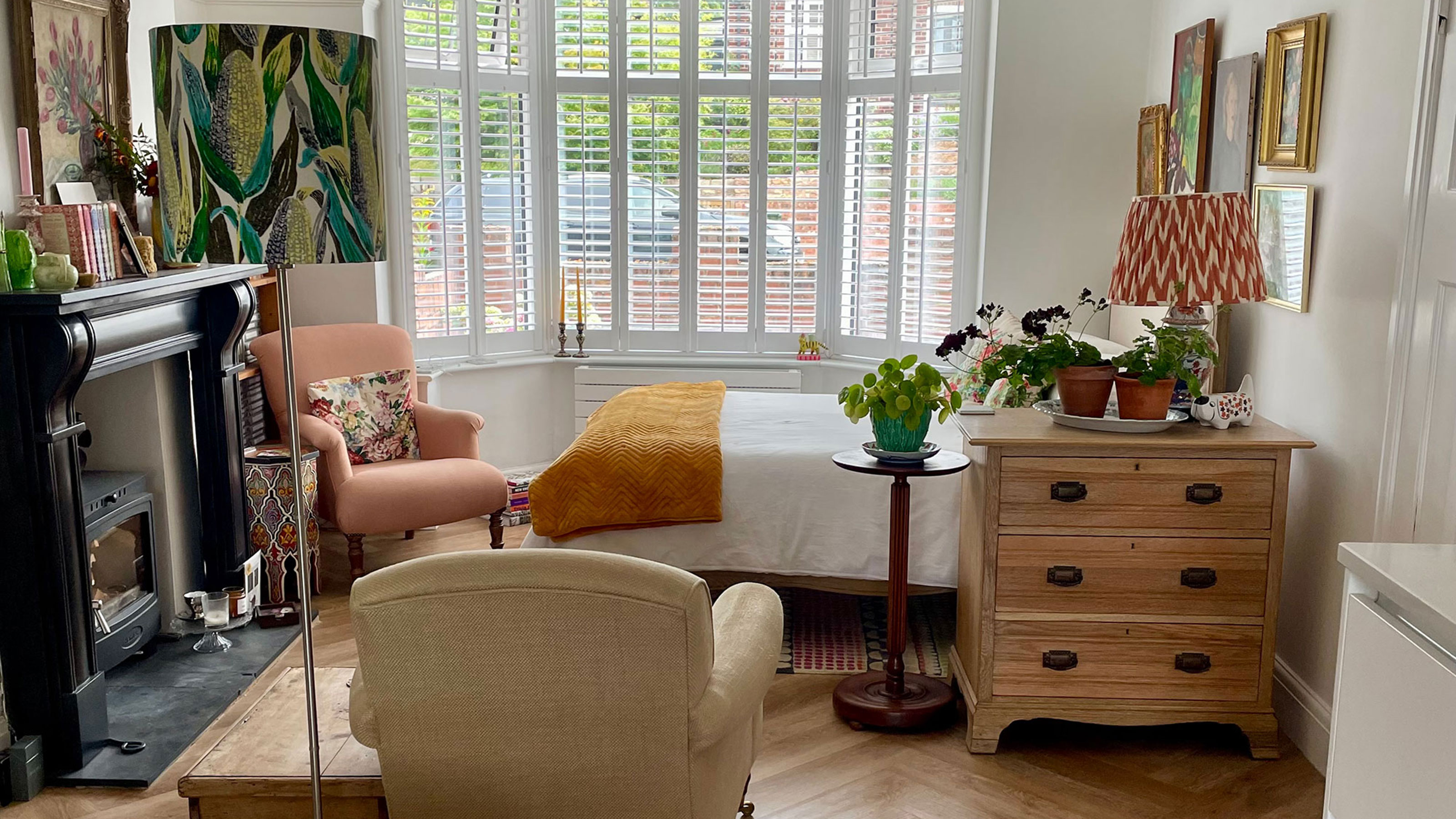 Bed by bay window, separated from rest of room with chest of drawers, side table, armchair and floor lamp
